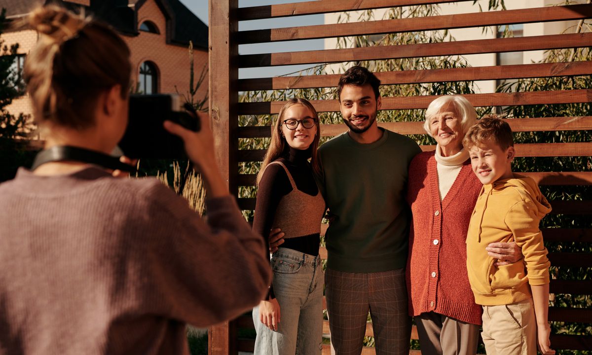 A multigenerational family smiling for a photograph in a sunny garden.